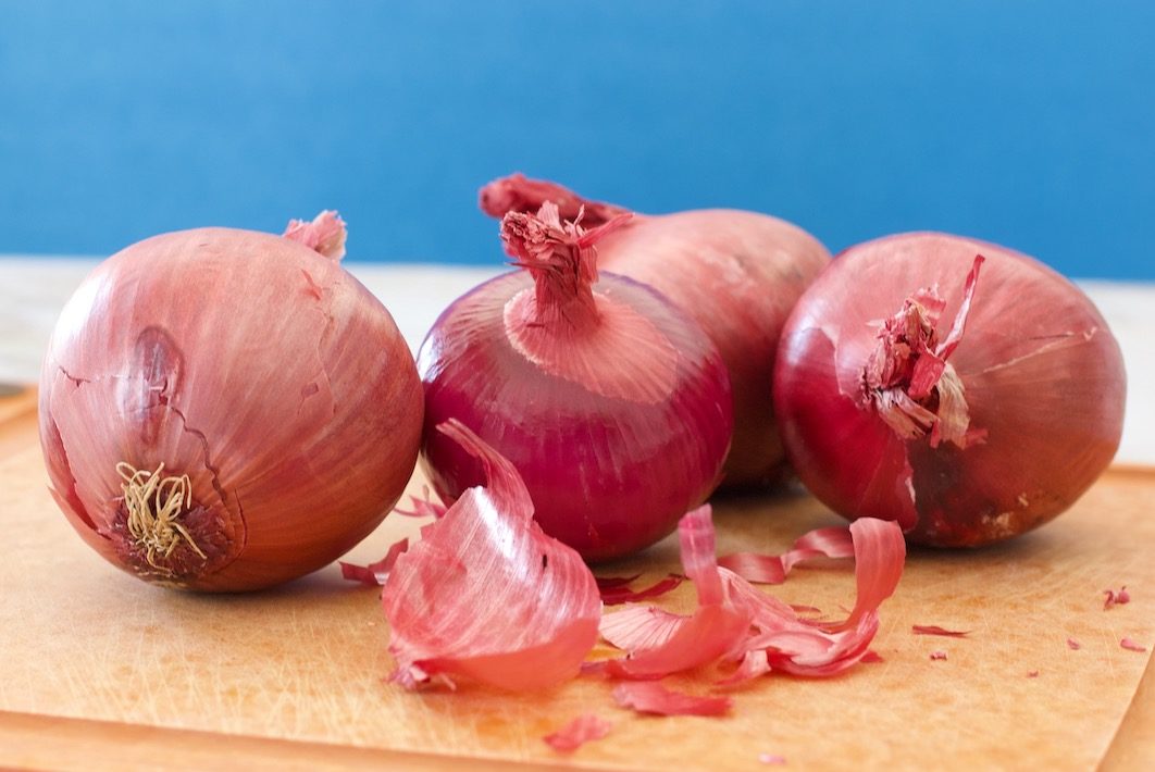 Four red onions on a cutting board with onion peels coming off