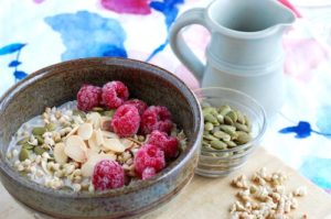 Sprouted buckwheat porridge served in a bowl, garnished with raspberries, toasted almonds, hemp hearts and pumpkin seeds.